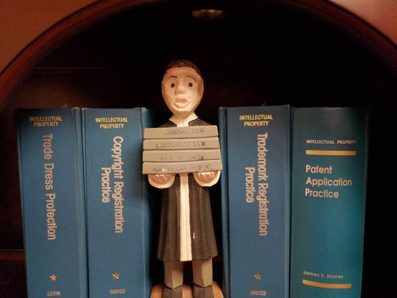 Wooden figure holding books in front of law books.