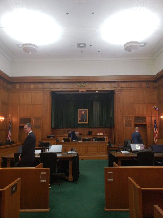 Courtroom interior with wood paneling, judge, and lawyers present.