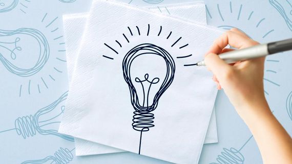 Hand drawing a lightbulb on a napkin with other lightbulb sketches in the background.