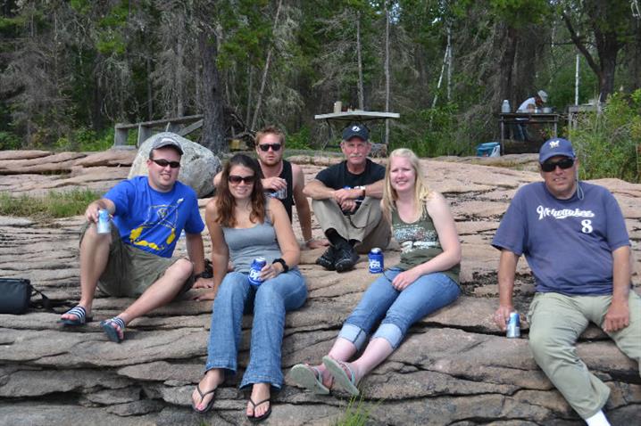 A family sitting on the Canadian Shield enjoying a fish fry of walleye for a shore lunch at Oak Lake Lodge.