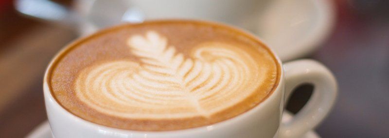 A close up of a cup of cappuccino with a leaf design on the foam.