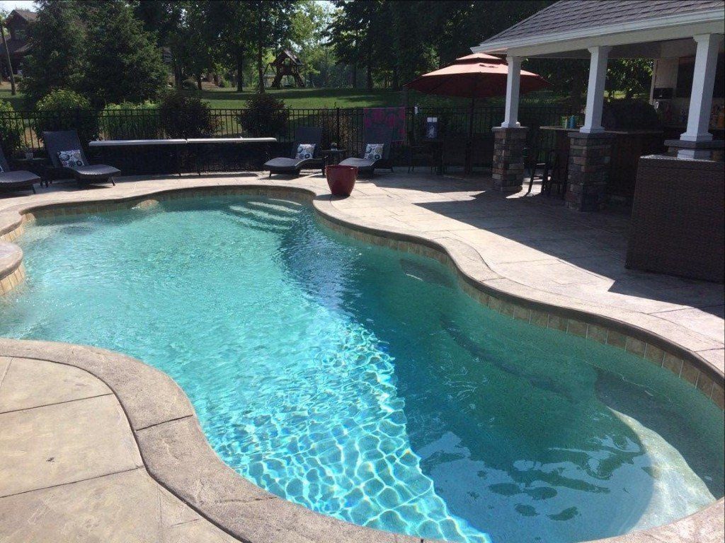 Curved backyard swimming pool with clear blue water, stone deck, and covered patio area