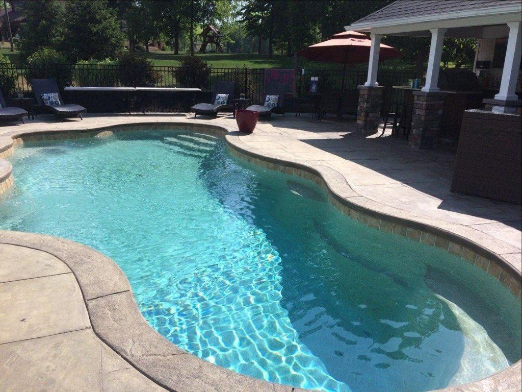 Backyard swimming pool with clear blue water, patio seating, and a shaded deck area