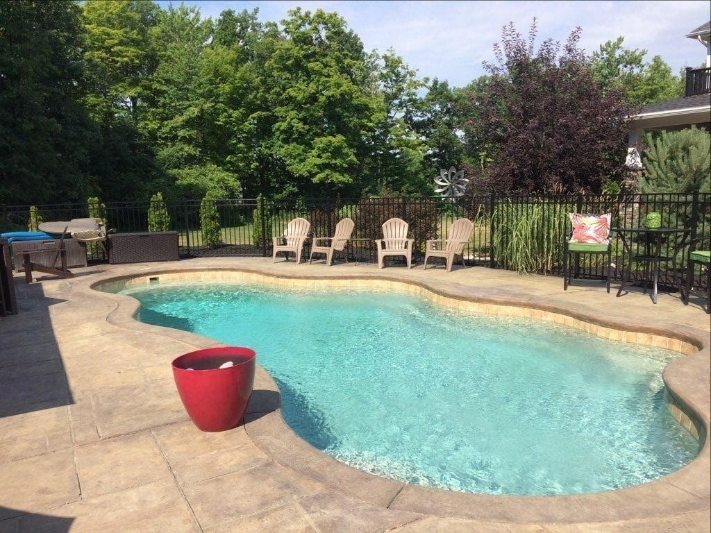 Backyard pool with turquoise water, red planter, chairs, and trees in the background