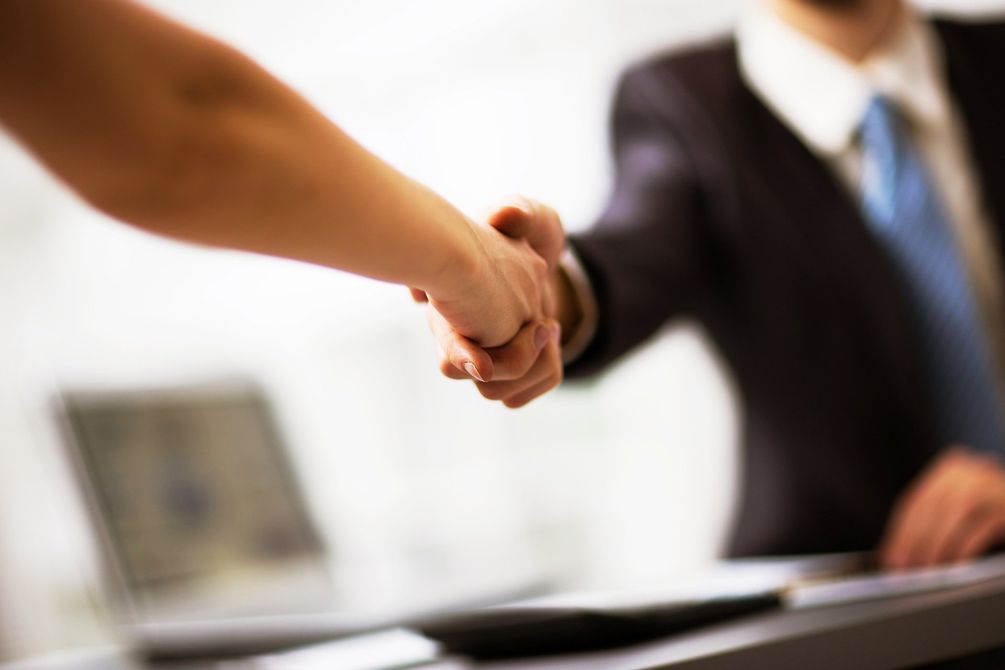 Stretta di mano tra due persone durante una riunione di lavoro, con uno sfondo sfocato di un ufficio.