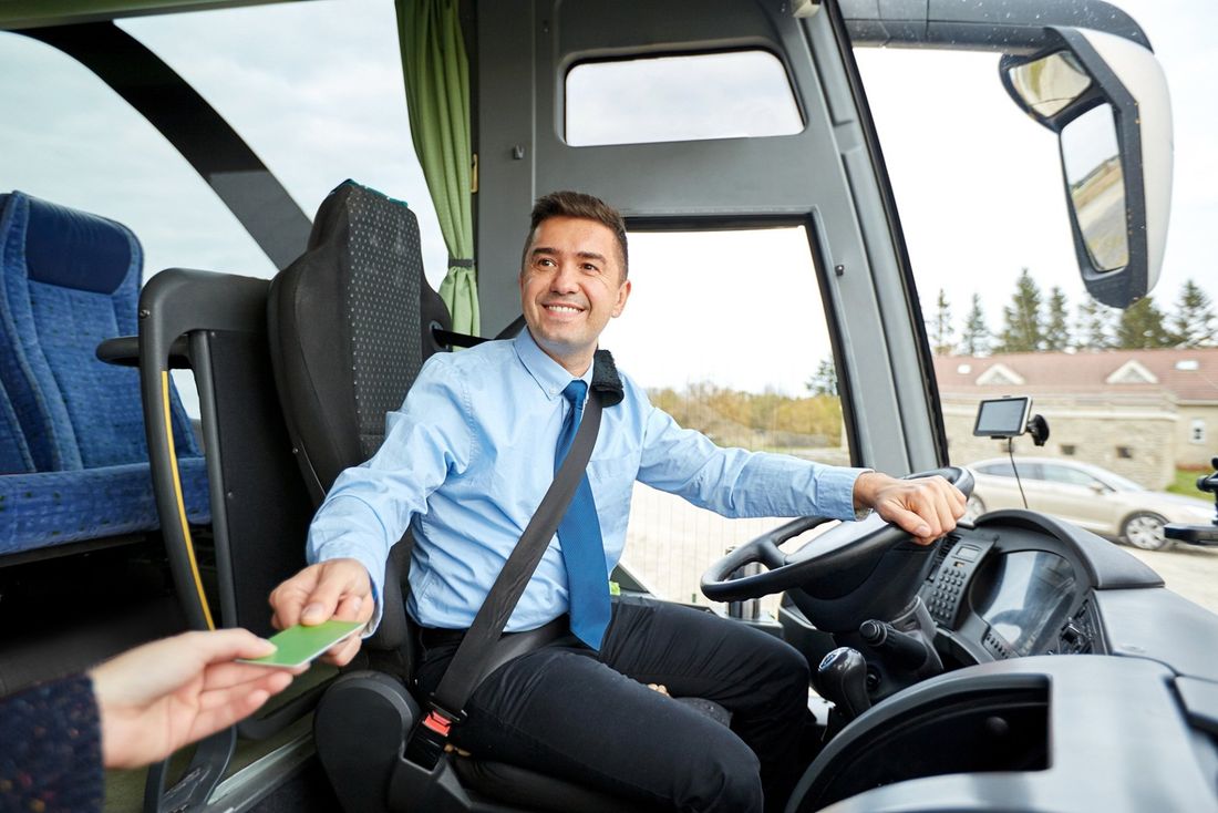 L'autista dell'autobus sorride e riscuote il biglietto da un passeggero vicino alla parte anteriore del mezzo.