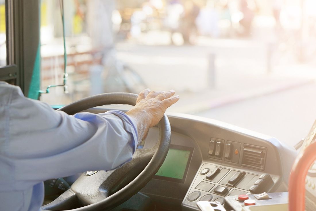 Le mani dell'autista dell'autobus sul volante e sul pannello di controllo all'interno di una cabina illuminata dal sole.