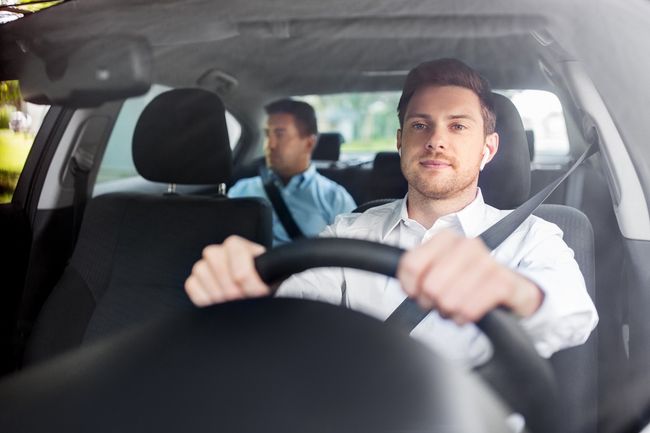 Un conducente tiene il volante in un'auto, con un passeggero seduto sul sedile posteriore.