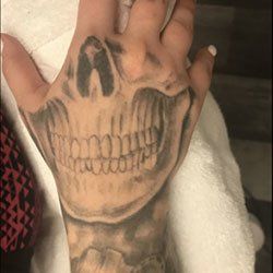 A close up of a person 's hand with a skull tattoo on it.