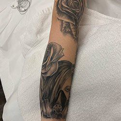 A black and white tattoo of a woman with roses on her arm.