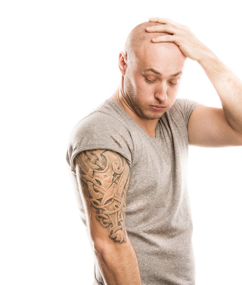 A bald man with a tattoo on his arm is holding his head.