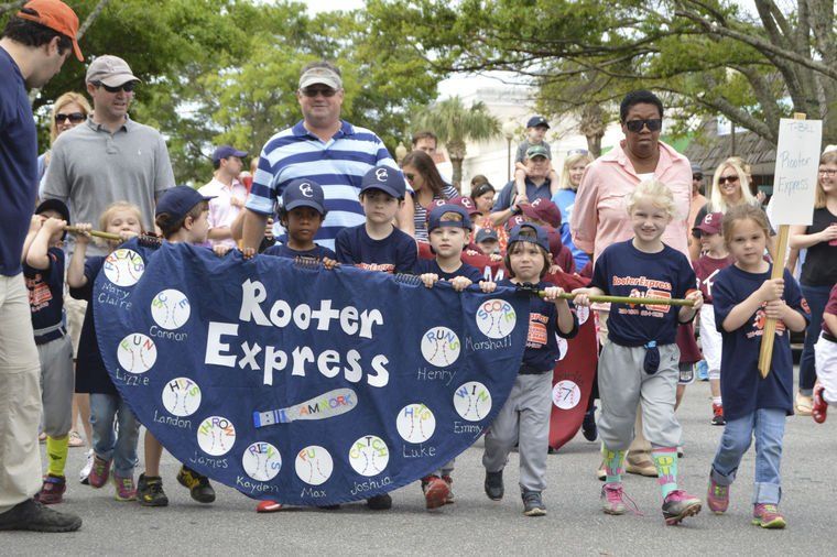 Children in baseball uniforms parade with a banner reading 
