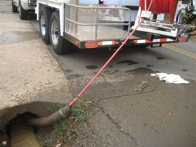Sewer cleaning truck with hose inserted into a drain near a street curb.