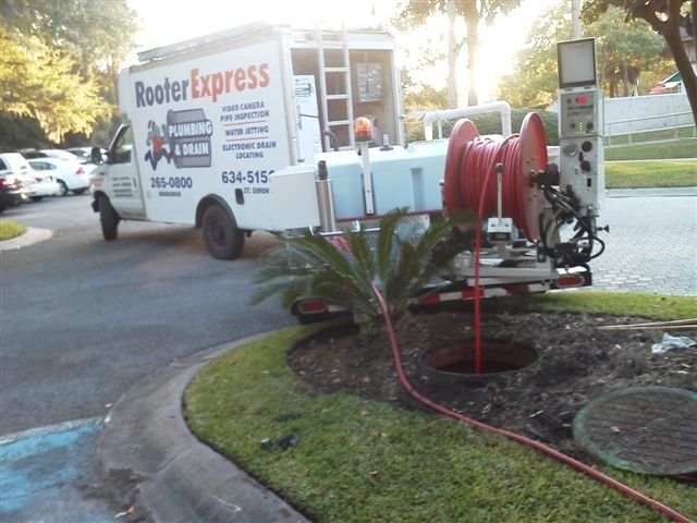 Rooter Express truck with hose extended into open manhole on a grassy patch.