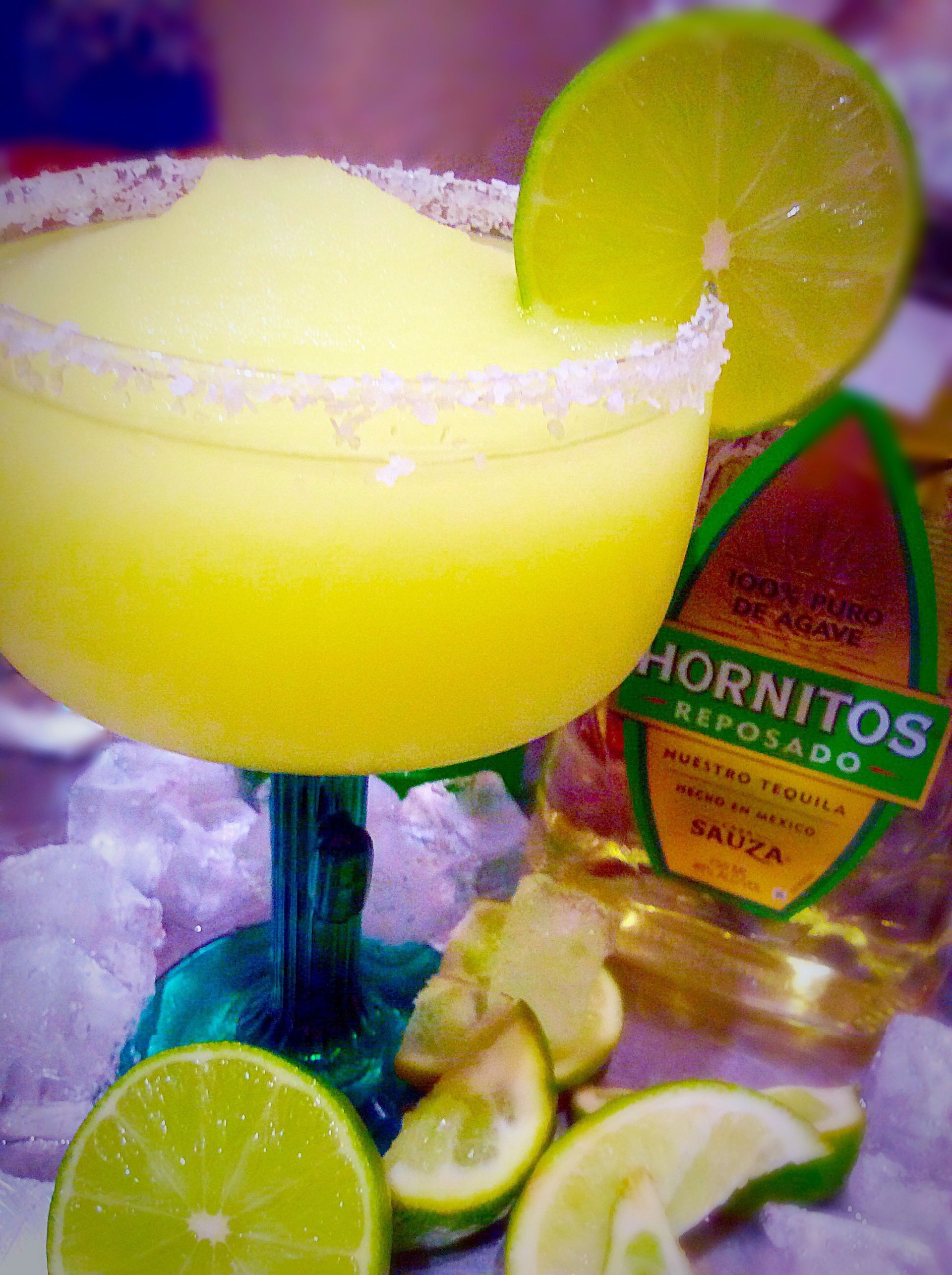 Frosted margarita in a salt-rimmed glass, lime garnish, Hornitos Reposado tequila bottle, and lime wedges.