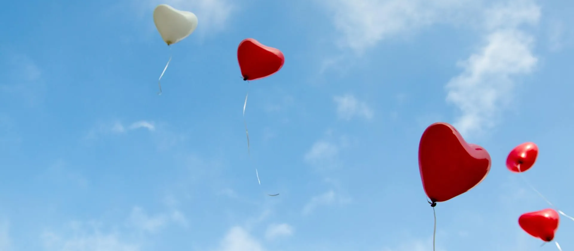 A group of heart shaped balloons are flying in the sky.