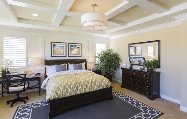 Bedroom — Springfield, OR — Northwest Home Furnishings A bedroom featuring a dark wood bed with a yellow patterned quilt, a desk, a dresser with a mirror, and a coffered ceiling.