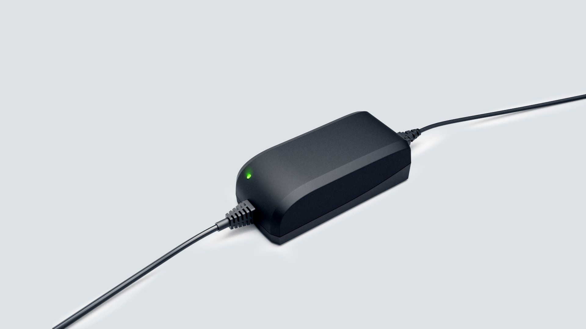 A black charger with a green light on it is sitting on a white surface.