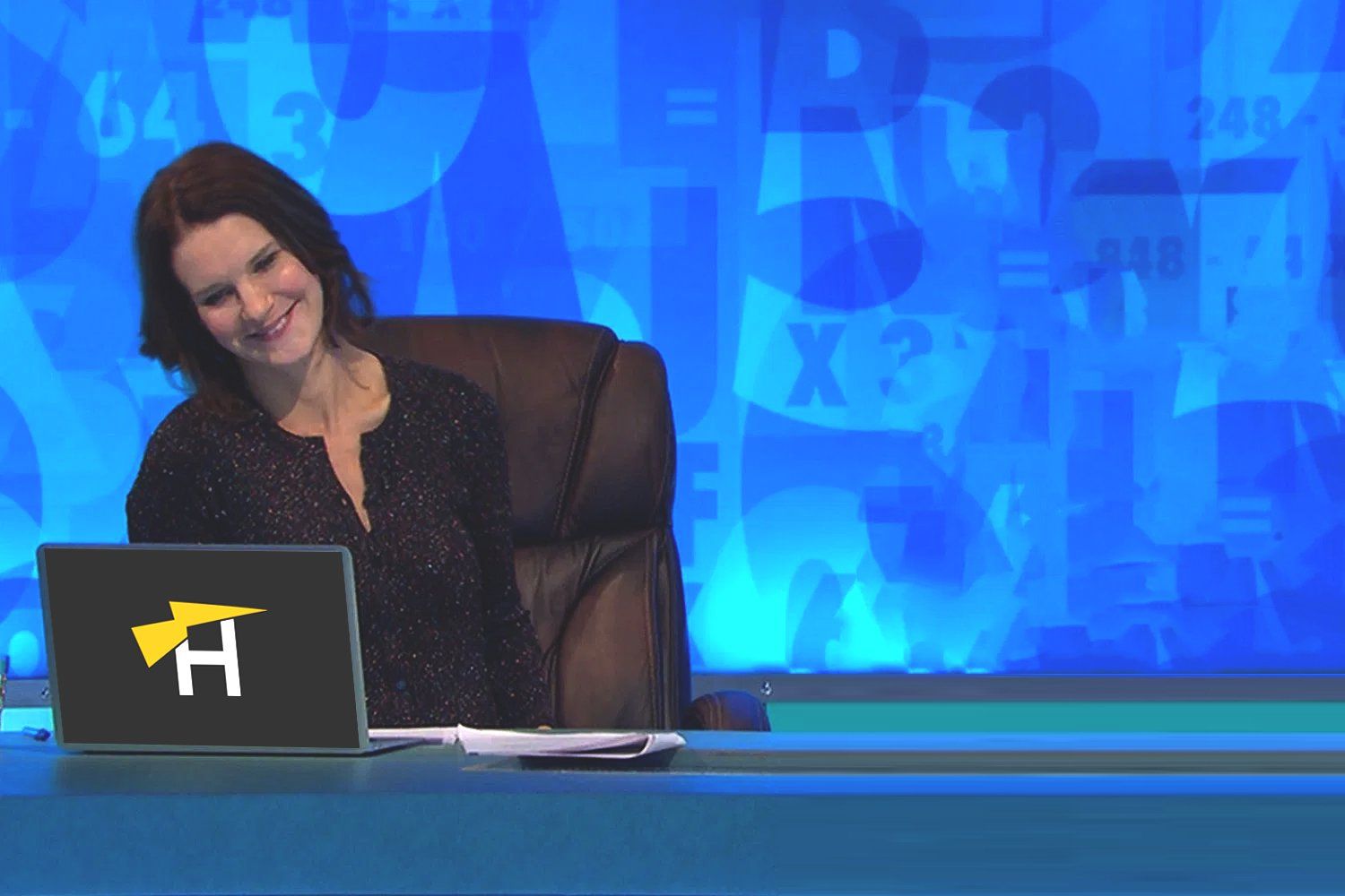 A woman is sitting in front of a laptop with the letter h on it