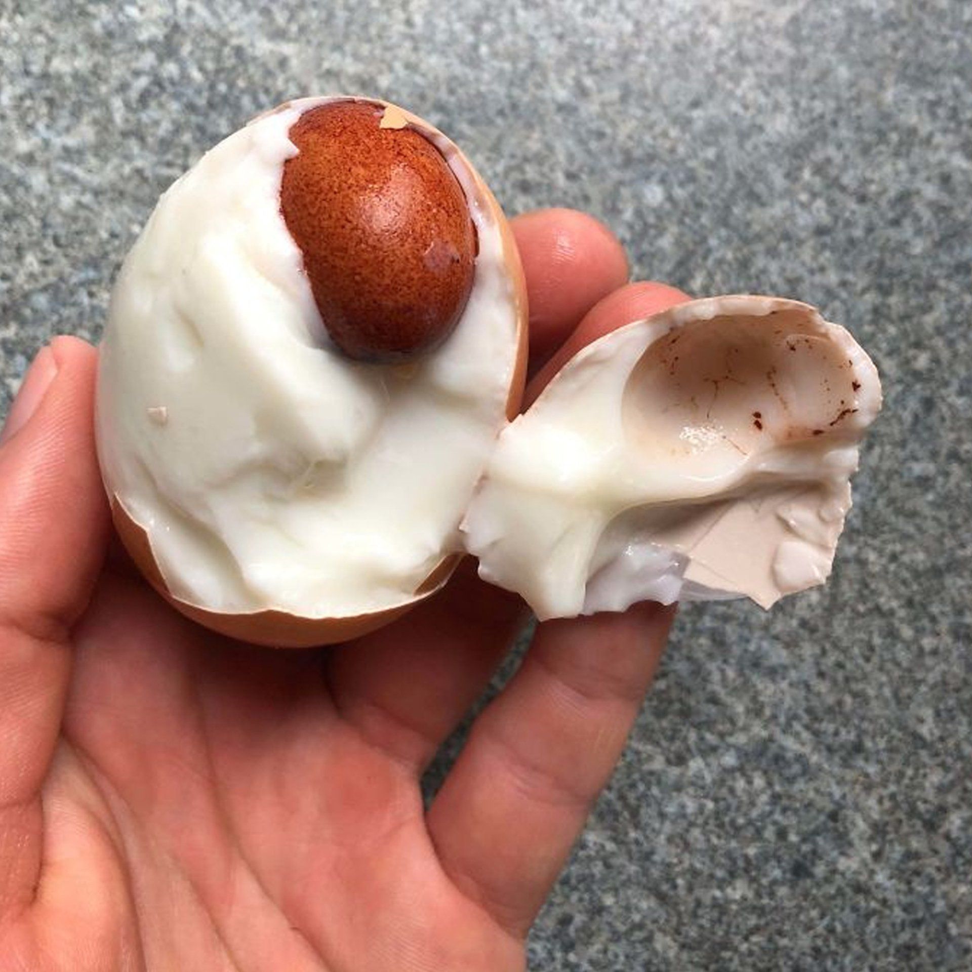 A person is holding a broken egg in their hand with another egg inside