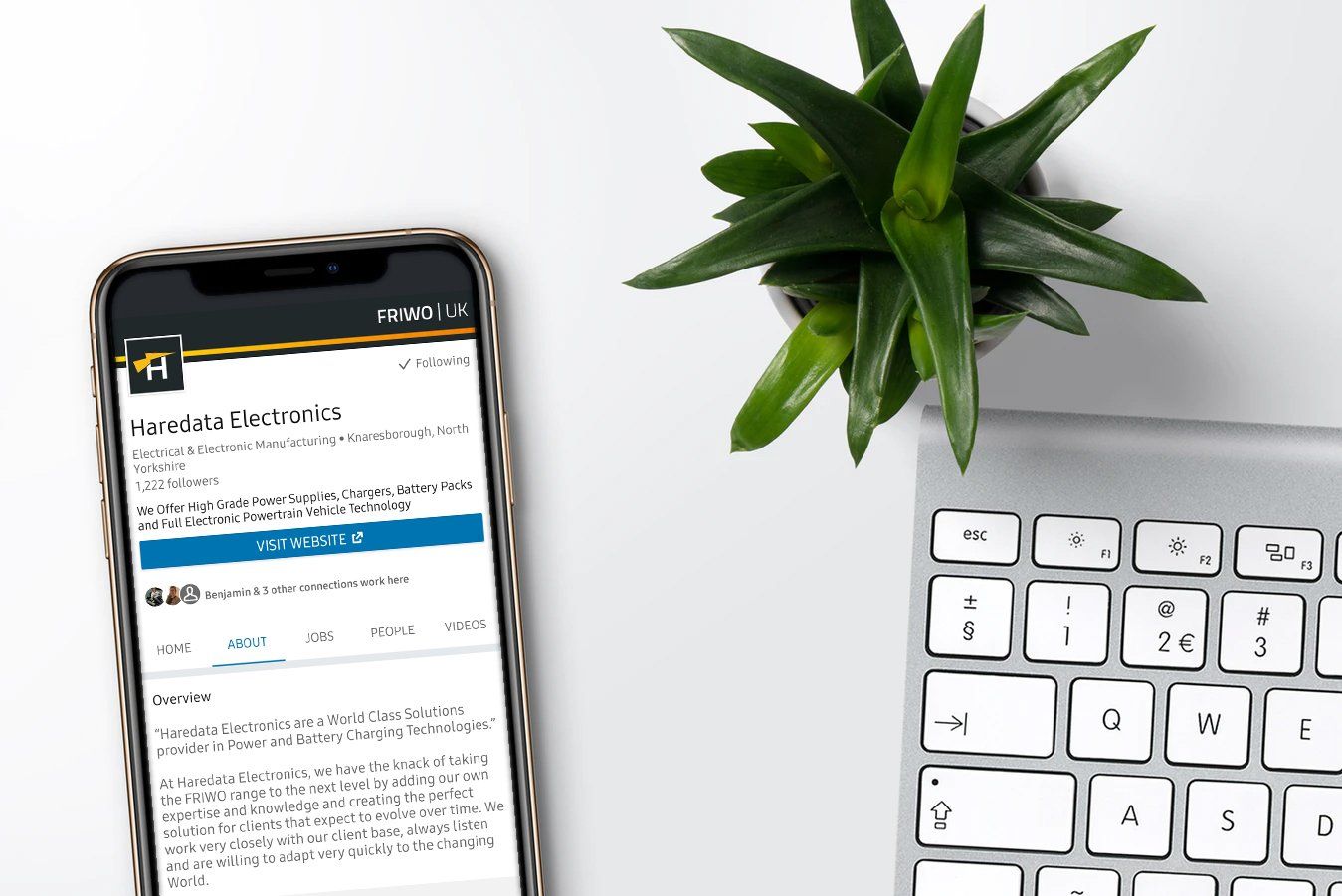 A cell phone is sitting next to a laptop and a potted plant.