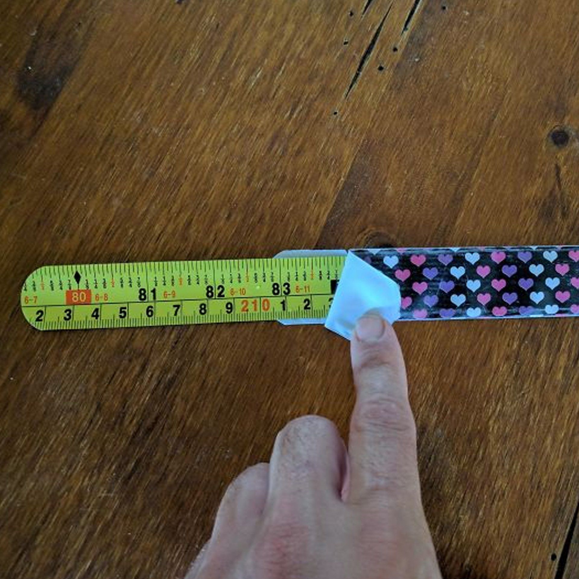 A person is measuring something with a tape measure that has hearts on it