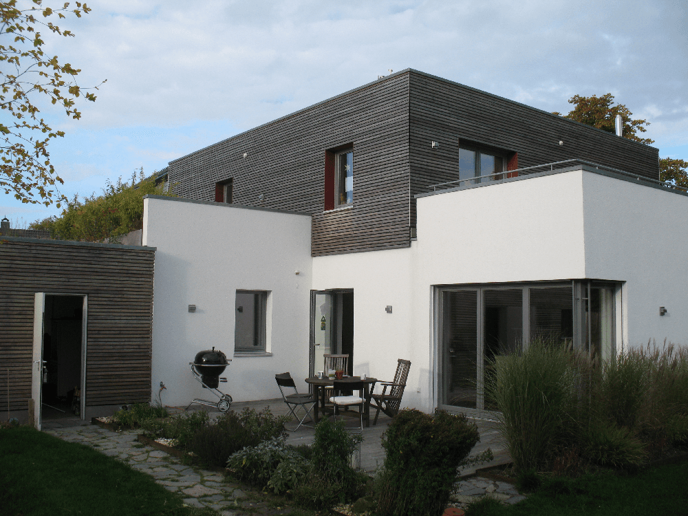 Modernes Haus mit weißen Wänden, dunkelgrauem Dach und Sitzbereich im Freien.