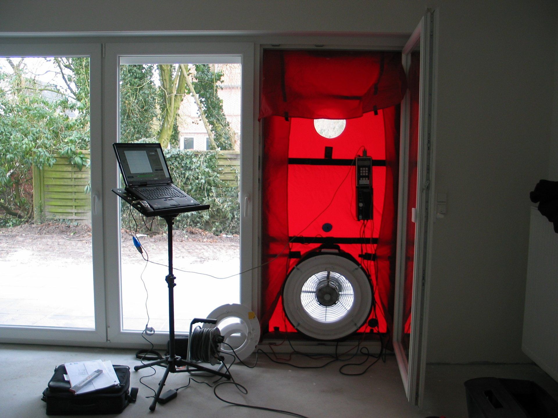 Ein Blower-Door-Testaufbau in einem Türrahmen mit einem Laptop auf einem Stativ.