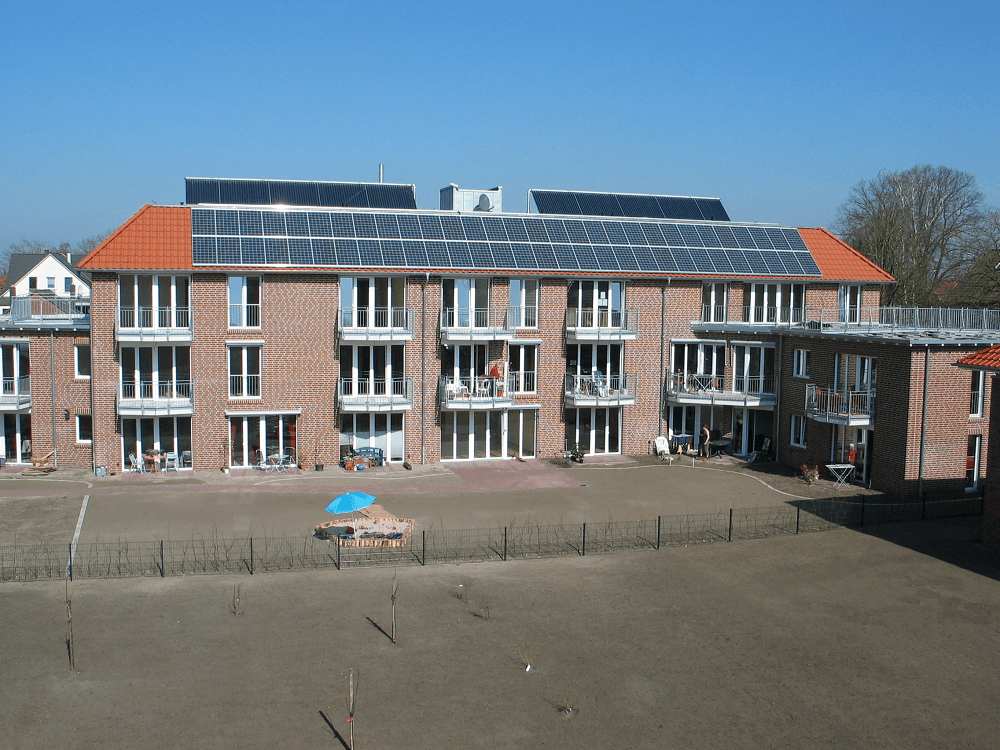 Mehrfamilienhaus aus Backstein mit Solaranlage auf dem Dach und mehreren Balkonen.