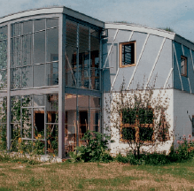 Modernes Haus mit geschwungenem Dach und großen Glasfenstern; gelegen in einem grasbewachsenen Garten.