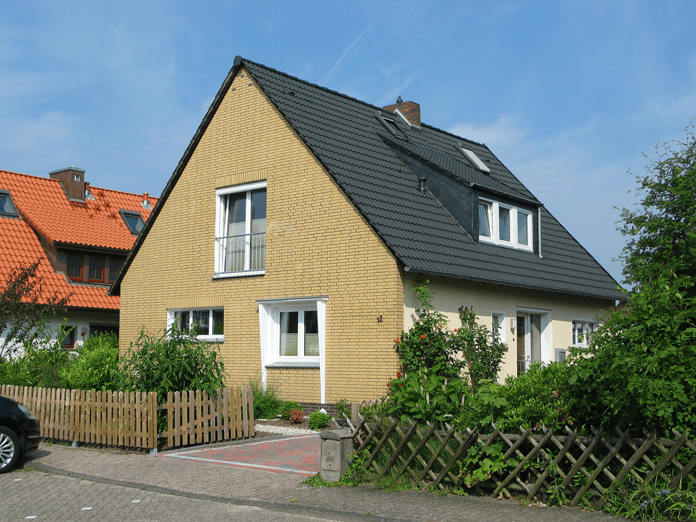 Gelbes Haus mit dunklem Dach und kleinem Holzzaun an einem sonnigen Tag.