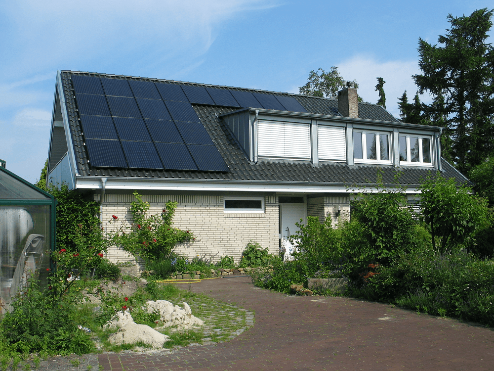 Haus mit Solarpaneelen auf dem Dach, Dachgauben und üppiger Gartengestaltung.
