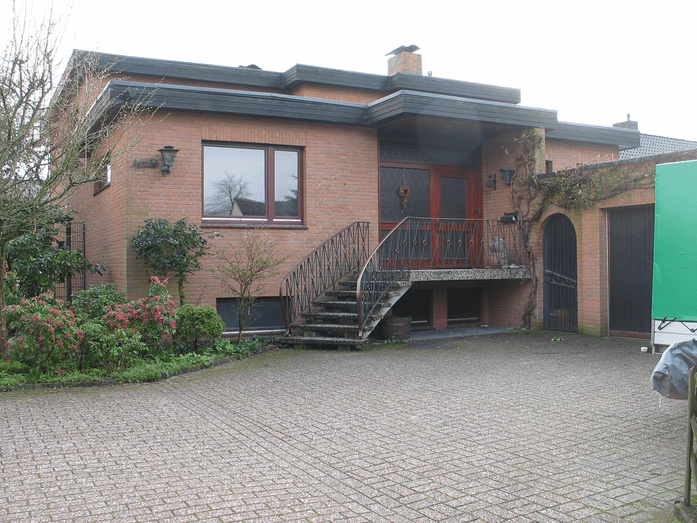 Backsteinhaus mit kleinem Balkon, geschwungener Treppe und angebauter Garage.