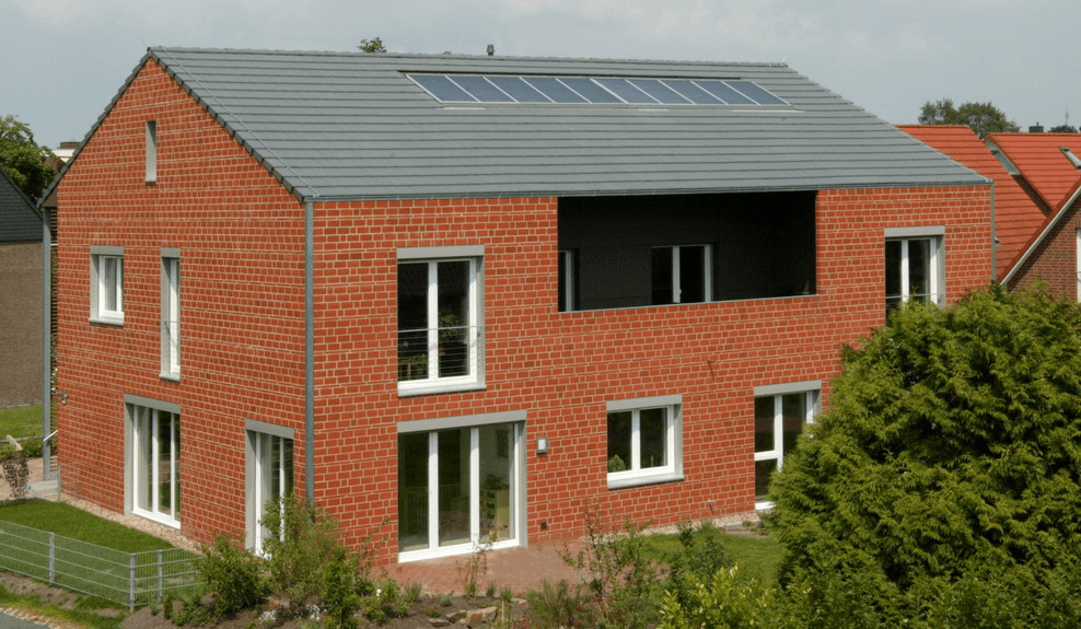 Zweistöckiges Backsteinhaus mit grauem Dach, Fenstern und Balkon. Solaranlage auf dem Dach.