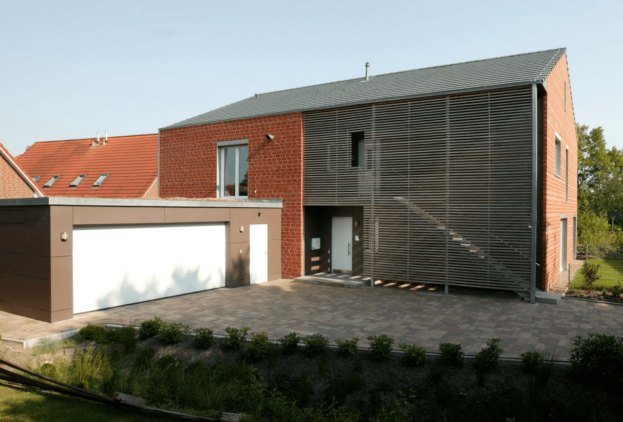 Modernes Backsteinhaus mit Lamellenfassade, Garage und gepflasterter Auffahrt.