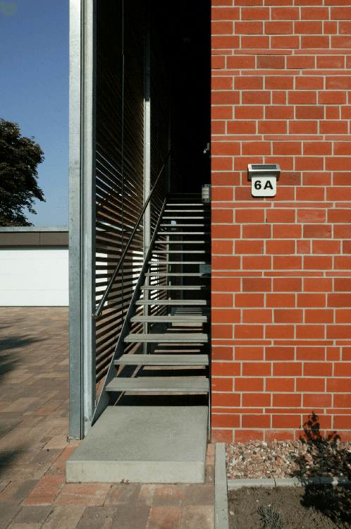 Außenansicht eines Gebäudes mit roter Backsteinmauer und nach oben führender Metalltreppe; Türnummer ist 6A.