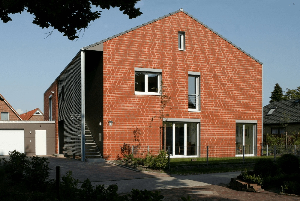 Modernes Backsteinhaus mit Metallverkleidung, Fenstern und kleinem Giebel.