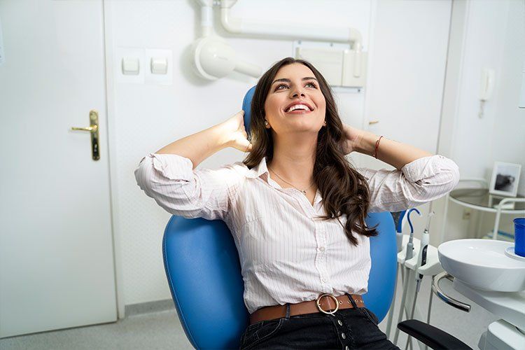 A woman is sitting in a dental chair with her hands behind her head.
