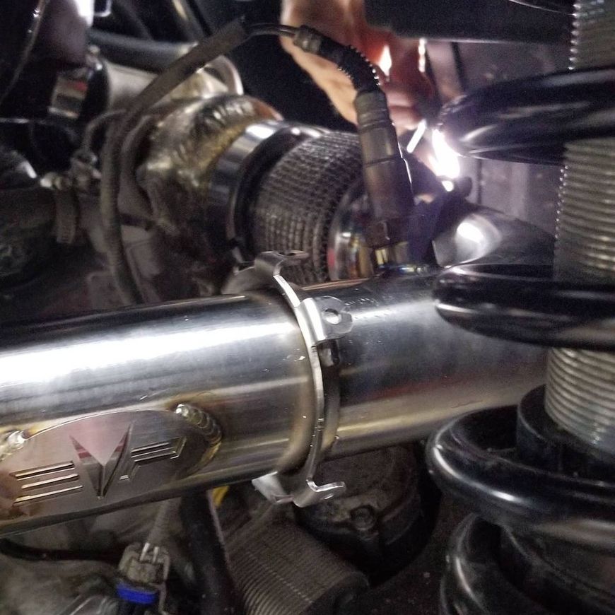 An O2 sensor installed in a stainless steel automotive exhaust pipe near a turbocharger and suspension spring.