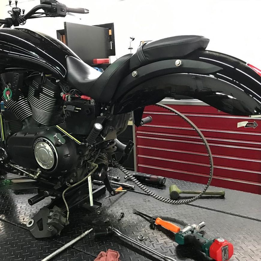A black motorcycle with its rear wheel removed sits on a workshop lift, with tools scattered nearby.