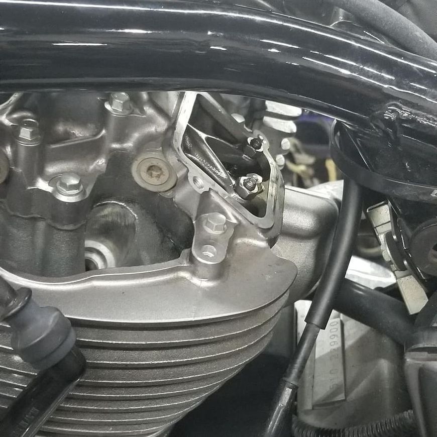 A close-up view of an exposed motorcycle engine cylinder head with a metal valve cover removed.