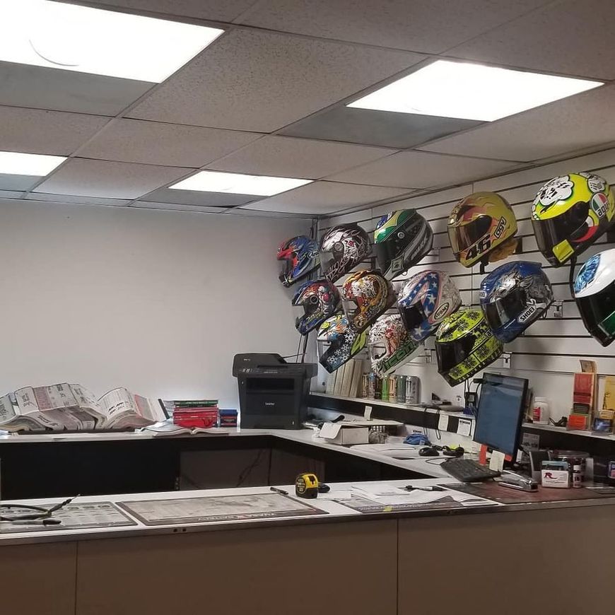 A row of colorful motorcycle helmets displayed on a wall rack in a workspace with a desk and computer equipment.