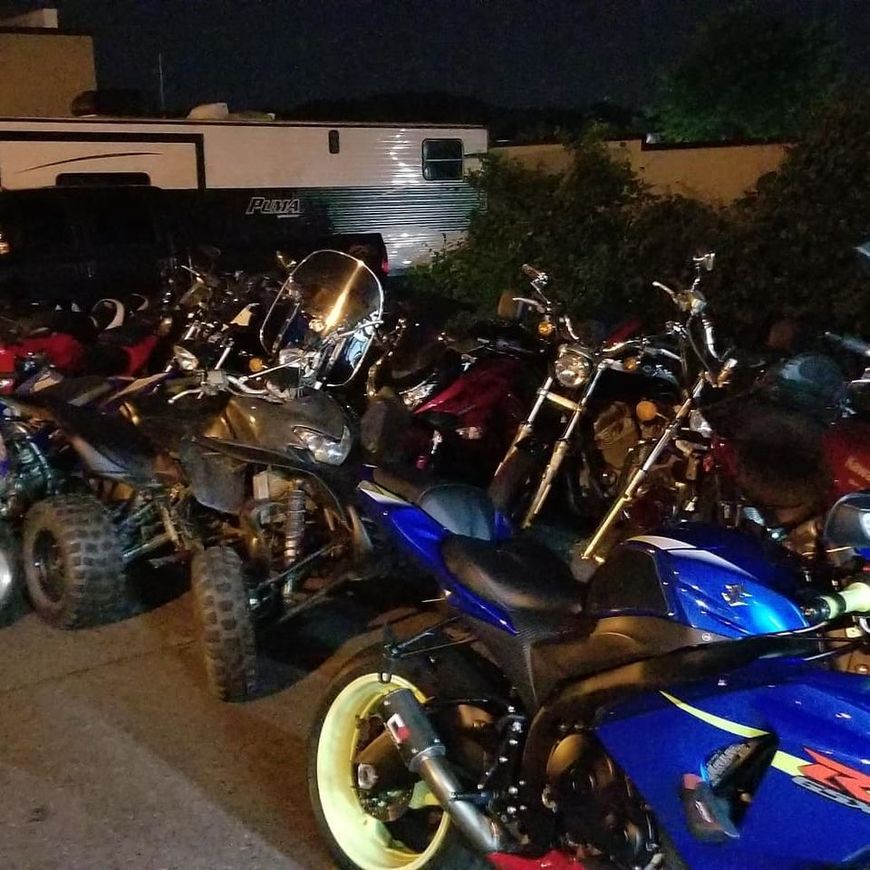 A blue Suzuki sportbike, a gray ATV, and several other motorcycles parked together outside at night.