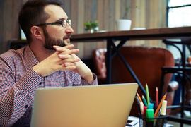 Individual with folded hands and and open laptop looking to left side
