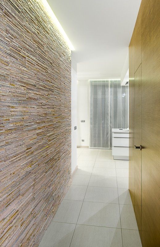 Schmaler Flur mit strukturierter Steinwand, heller Holztür und weißem Fliesenboden.