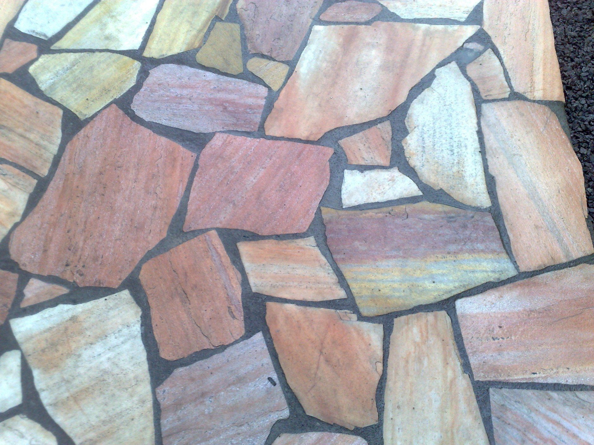 Unregelmäßig geformte Sandstein-Terrassenplatten mit grauem Mörtel in Braun-, Orange- und Goldtönen.