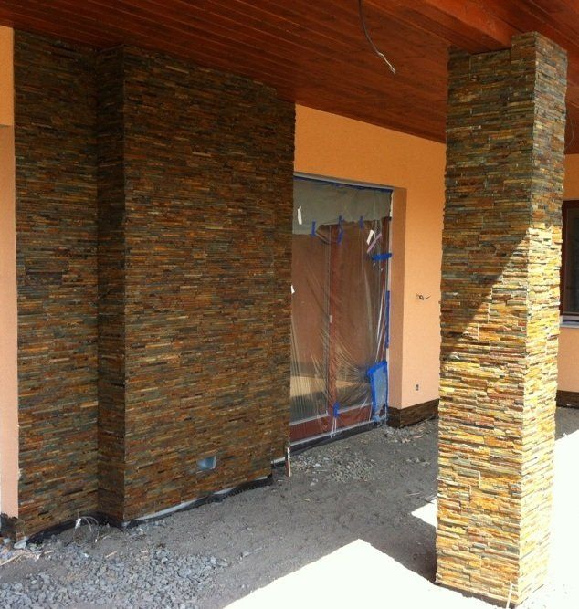 Außenfassade mit strukturierten Steinsäulen und -wänden, orangefarbenem Stuckhintergrund und Holzdecke.