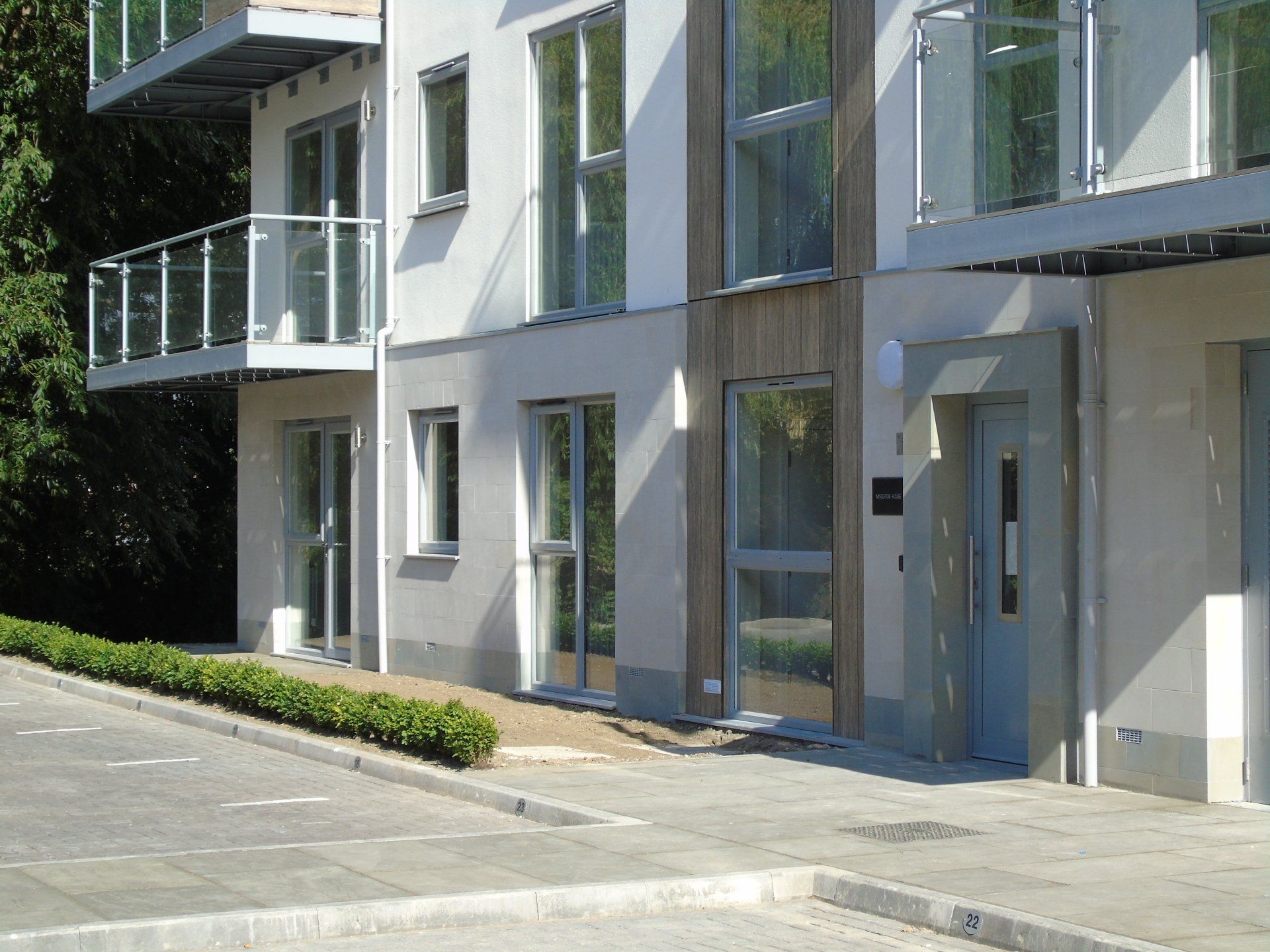 Modernes Apartmentgebäude mit Balkonen, Glasgeländern und Eingang mit grauer Tür.