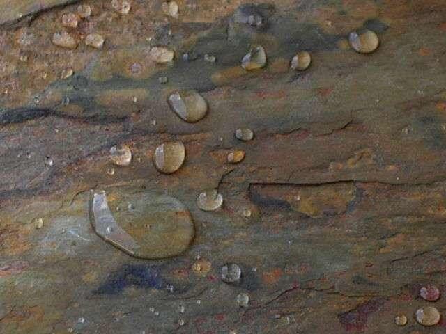 Wassertropfen auf einer rauen, mehrfarbigen Steinoberfläche.