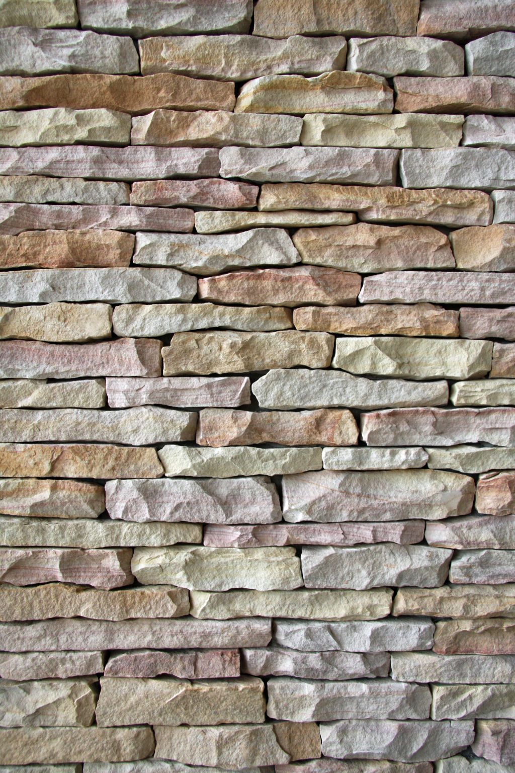 Steinmauer aus rechteckigen Steinen in den Farben Beige, Rosa und Grau.